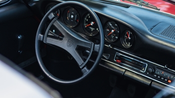 Panel de instrumentos de un Porsche clásico con volante negro, indicadores analógicos y una radio antigua.