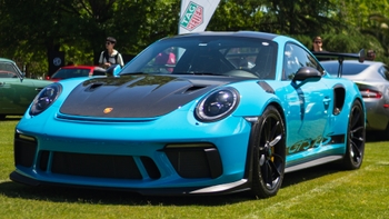 Porsche 911 GT3 RS turquesa con capó de fibra de carbono en exhibición al aire libre, destacando su diseño deportivo y alerón trasero.