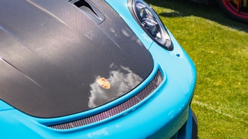 Porsche 911 GT3 RS turquesa con capó de fibra de carbono en exhibición al aire libre, destacando su diseño deportivo y alerón trasero.