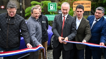 Varias personas, incluyendo algunos hombres en traje y otros casuales, cortando una cinta tricolor (rojo, blanco, azul) para inaugurar una estación de carga Porsche en Chile, con un Porsche eléctrico visible al fondo.