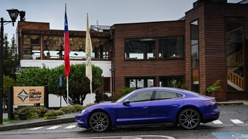 Porsche Taycan morado estacionado con banderas y calle mojada.