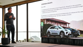 Hombre presentando la estrategia de electromovilidad y puntos de carga en Chile, con imágenes del Porsche Macan eléctrico en pantalla.