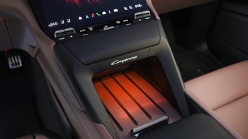 Detalle de la consola central de un Porsche Cayenne eléctrico, mostrando la bandeja de carga inalámbrica iluminada en naranja y el logo "Cayenne".