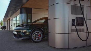 Porsche Macan eléctrico verde estacionado y cargando en una moderna estación, con el cable conectado al pilar de carga.