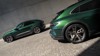 Dos Porsche verdes, un Macan eléctrico y un Taycan Cross Turismo, estacionados en una superficie adoquinada frente a una pared.