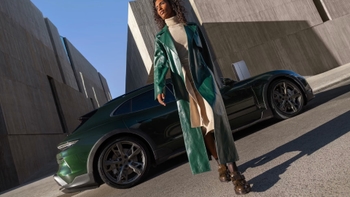 Mujer elegante con abrigo verde posa junto a un Porsche 911 Dakar verde oscuro, destacando el diseño robusto y deportivo del vehículo.