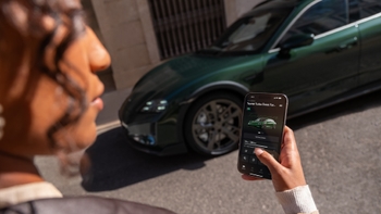 Persona observando la pantalla de un smartphone con la aplicación Porsche, mostrando los detalles del modelo Taycan Turbo Cross Turismo, con el vehículo verde en segundo plano.