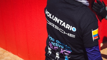Detalle de la camiseta de un voluntario de Porsche con la bandera de Colombia, mostrando el logo de "Voluntario Porsche" y un mensaje de acción colectiva.