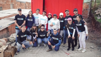 Grupo de voluntarios de TECHO posando frente a una vivienda en construcción, mostrando apoyo a la comunidad.