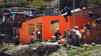 Grupo de voluntarios trabajando en la construcción de viviendas en una zona rural, con algunos vistiendo camisetas de TECHO.