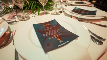 Mesa elegantemente dispuesta con menú del evento "30 años Porsche en Colombia" sobre un plato blanco.