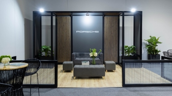 Lounge de Porsche con sofás grises, plantas y el logo de Porsche en la pared.