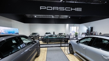 Variedad de modelos Porsche, incluyendo un 911 verde y Macan, exhibidos en un evento bajo el logo de Porsche.