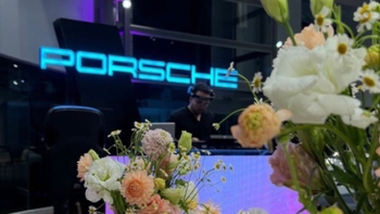 Foto en ángulo tomando en primer detalle a flores y mostrando de fondo el logo de Porsche luminoso.