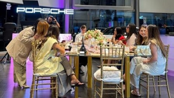 Participantes e influencers interactuando en una mesa decorada frente al logo luminoso de Porsche.