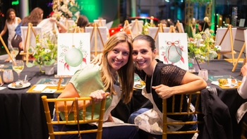 Dos mujeres sonrientes posando en un evento "Season of Wonder" de Porsche, con lienzos pintados y un ambiente festivo.