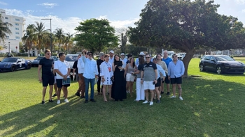 Grupo de participantes posando en un césped junto a varios coches y palmeras durante el evento.