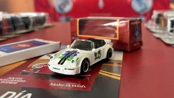 Un coche de juguete Porsche 911 Cabriolet blanco con el número 25, sobre material promocional de "Make A Wish".