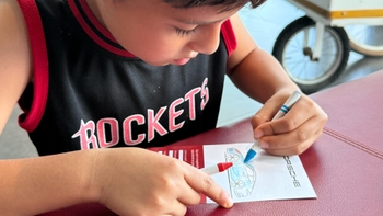 Primer plano de un niño con camiseta de "Rockets" concentrado coloreando un dibujo de un coche Porsche.