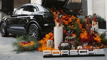 Porsche decorado con una ofrenda floral y elementos tradicionales del Día de Muertos, con letrero de Porsche en primer plano.