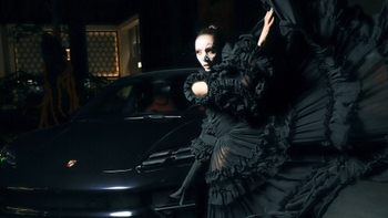 Vista lateral de un Porsche negro con la cajuela llena de flores de cempasúchil y elementos de una ofrenda del Día de Muertos.