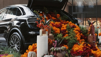 Porsche negro con la cajuela abierta, llena de flores de cempasúchil y elementos decorativos del Día de Muertos en una presentación visual impactante.