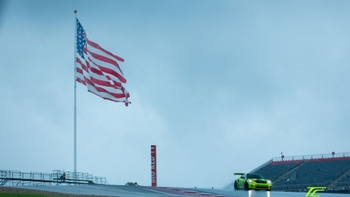 Lime green Porsche GT3 RS on track while the American flag waves
