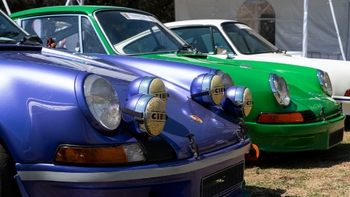 Porsche 911 clásico morado con faros auxiliares CIBIE y un 911 verde, exhibidos en un evento al aire libre.