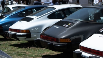Fila de Porsche 911 SC clásicos en azul, blanco y gris, mostrando sus partes traseras en un evento automovilístico.
