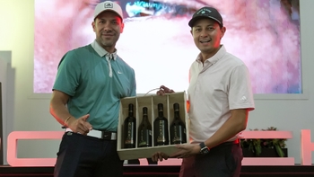 Dos hombres sonrientes, uno con polo verde y otro con polo rosa, sostienen una caja de vinos Don Luis como premio en un evento.