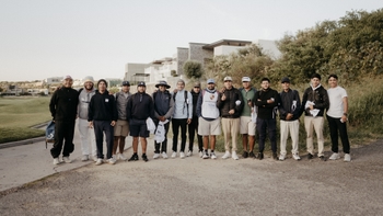 Grupo de golfistas posando juntos en un campo de golf, con un edificio moderno al fondo.
