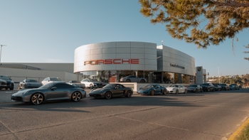 Fachada de concesionario Porsche con fila de autos Porsche estacionados al frente, mostrando variedad de modelos.
