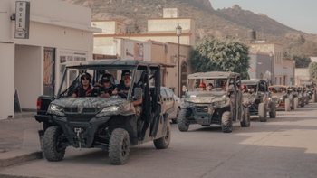 Grupo de personas conduciendo vehículos todo terreno (UTV) a través de un pintoresco pueblo con arquitectura colonial.
