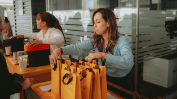 Dos mujeres organizando y disponiendo bolsas de regalo de 'Palacio de Hierro' en un mostrador durante un evento.