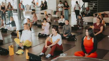 Mujeres sentadas en esterillas de yoga en un concesionario Porsche, escuchando a instructores durante un evento o clase.
