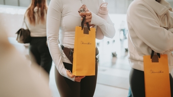 Primer plano de una persona sosteniendo una bolsa de regalo de 'Palacio de Hierro', un celular y una botella de agua.