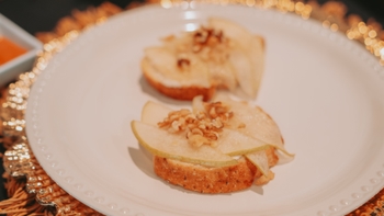 Dos tostadas gourmet con rodajas de pera, queso y nueces picadas sobre un plato blanco, con decoración festiva de fondo.
