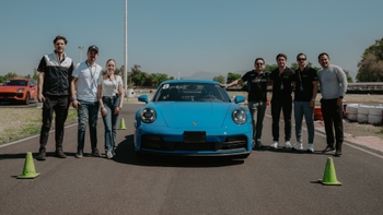 Un grupo de personas posa sonriente junto a un Porsche 911 azul en una pista de carreras con conos.