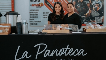 Dos mujeres sonrientes atienden el puesto de comida "La Panoteca", ofreciendo pan y repostería.