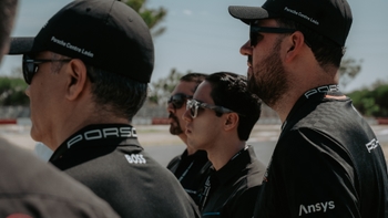 Grupo de hombres, algunos con gorras y camisetas de Porsche Centre León, observando atentamente en un evento al aire libre.