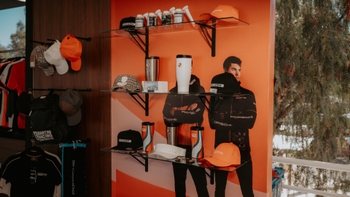 Exhibición de gorras, termos y ropa Porsche Design en estantes de una boutique con gráfica de marca.