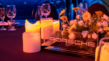 Centro de mesa con velas LED, arreglo floral y placa acrílica con la palabra Porsche en evento.