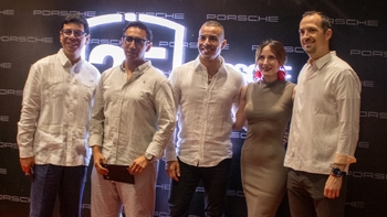 Grupo de cinco personas sonrientes, tres hombres y dos mujeres, posando frente a una pared con el logo de Porsche durante la inauguración.