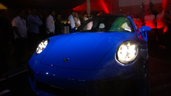 Un Porsche 911 azul vibrante con faros encendidos, presentado ante una audiencia durante la inauguración de Porsche Centre Mérida.