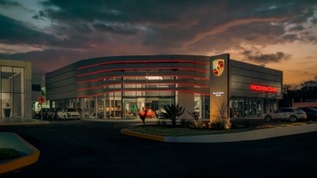 Exterior del Porsche Centre Mérida al atardecer, mostrando la arquitectura moderna con iluminación LED roja y varios vehículos Porsche en exhibición.