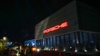 Fachada iluminada del Porsche Centre Mérida por la noche, destacando el letrero PORSCHE en rojo y la arquitectura moderna del concesionario.