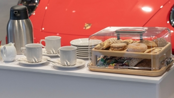 Mesa con desayuno, platos, tazas y comestibles al lado de un Porsche.