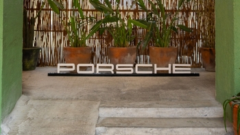 Logo de Porsche corporeo color blanco, entre paredes verdes y plantas.