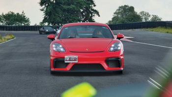 Vista frontal de un Porsche 718 Cayman GT4 rojo en una pista, con placa de Morelos, México, y otros autos en el fondo.
