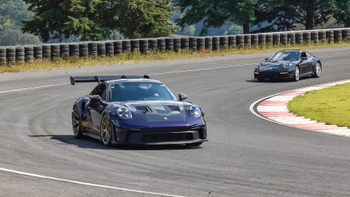Porsche 911 GT3 RS morado en primer plano, con otro Porsche negro detrás en una pista de carreras.